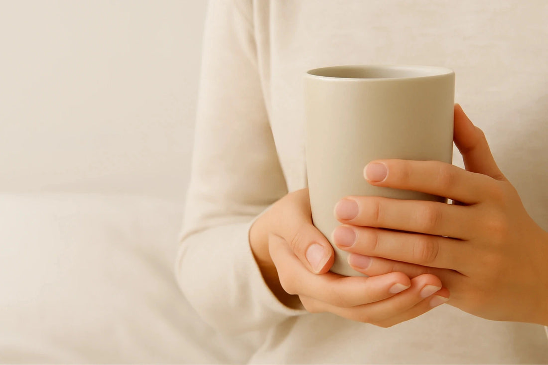 Person holding a white ceramic mug against a plain background