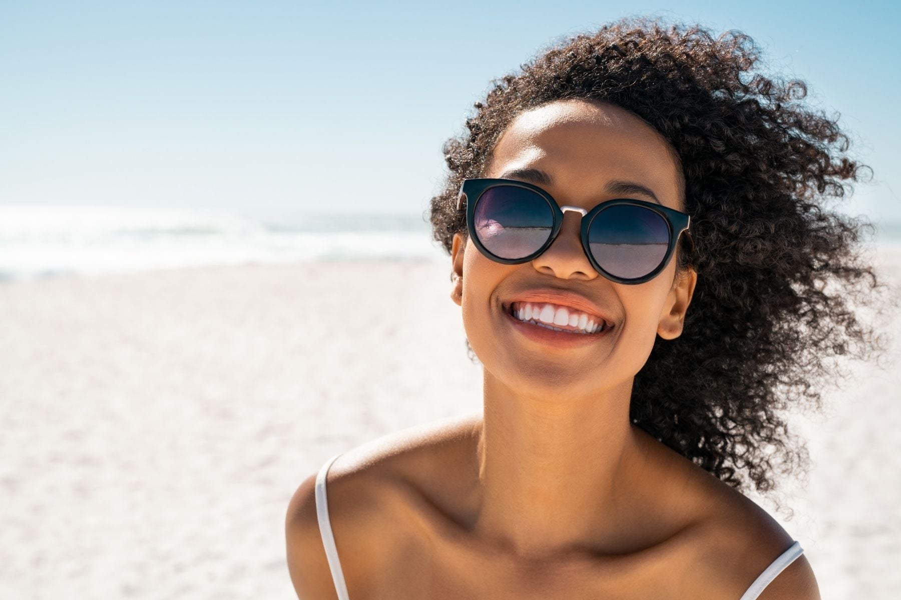 Woman wearing sunglasses on a beach with clear blue sky