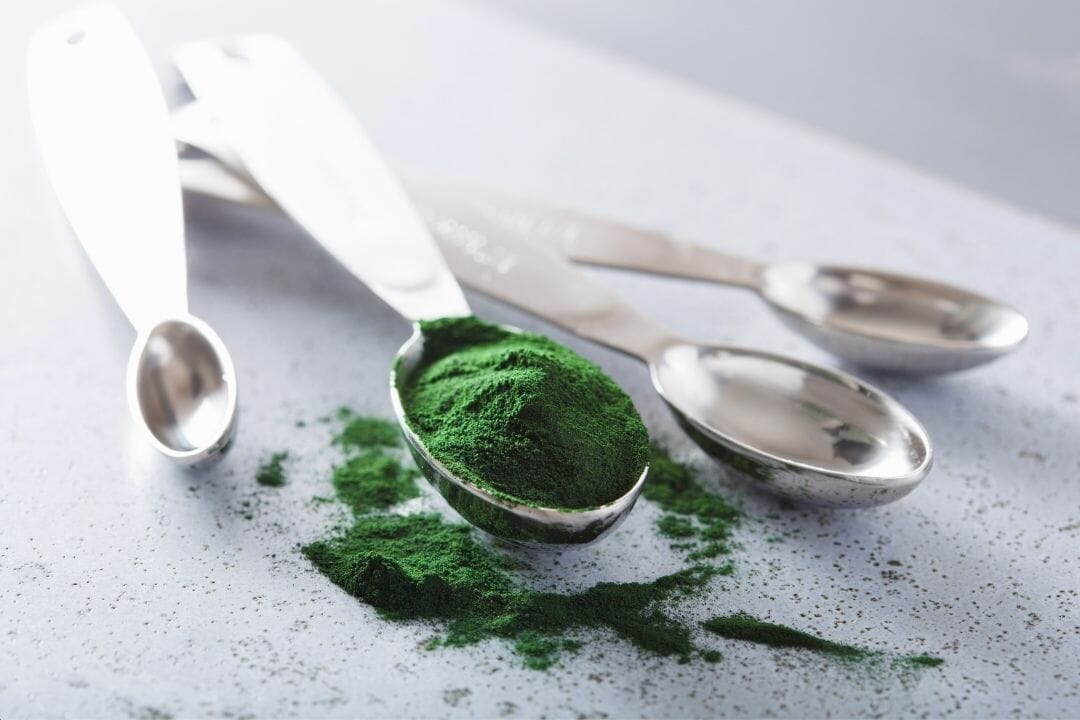Green powder on a metal spoon with additional spoons around on a light background