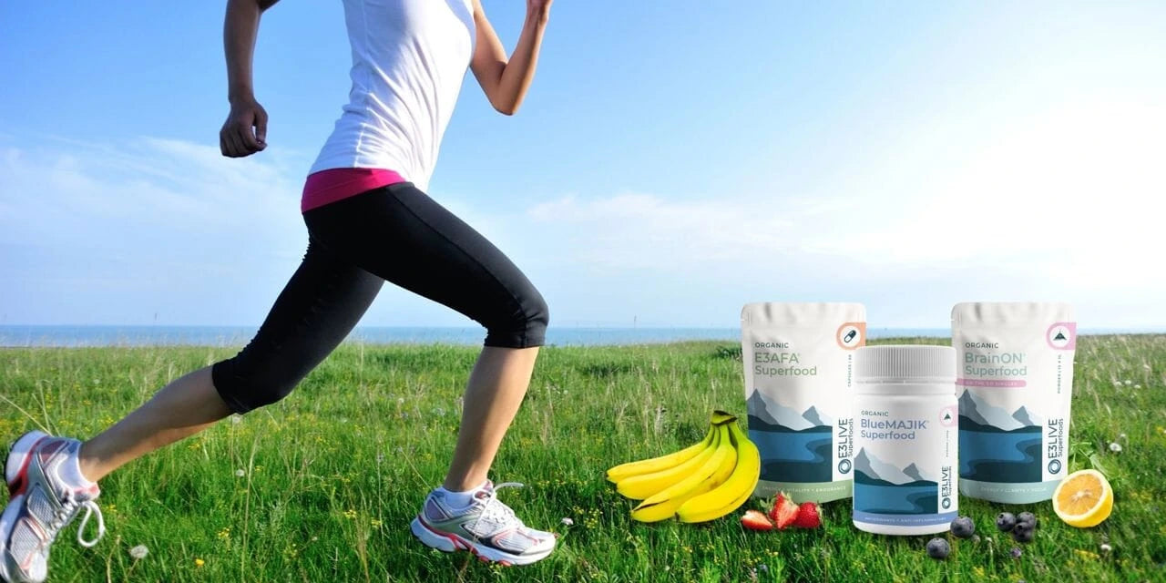 Person running outdoors with E3Live Superfodds protein powder containers and fruits on a grassy field